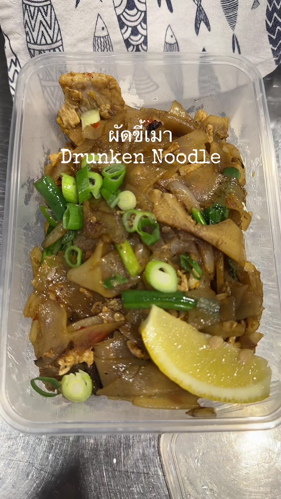 A takeaway container of drunken noodles, labelled in Thai and English