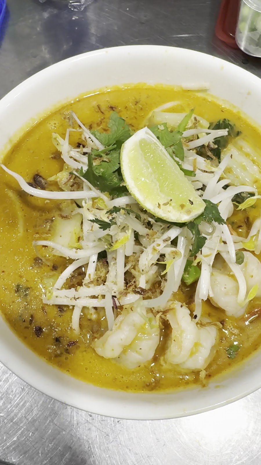 A bowl of prawn laksa topped with bean sprouts and lime