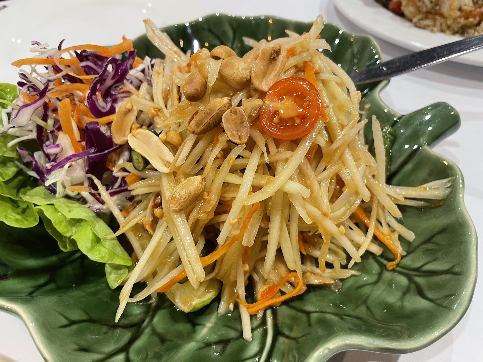 Green papaya salad with peanuts and tomato on a leaf-shaped plate